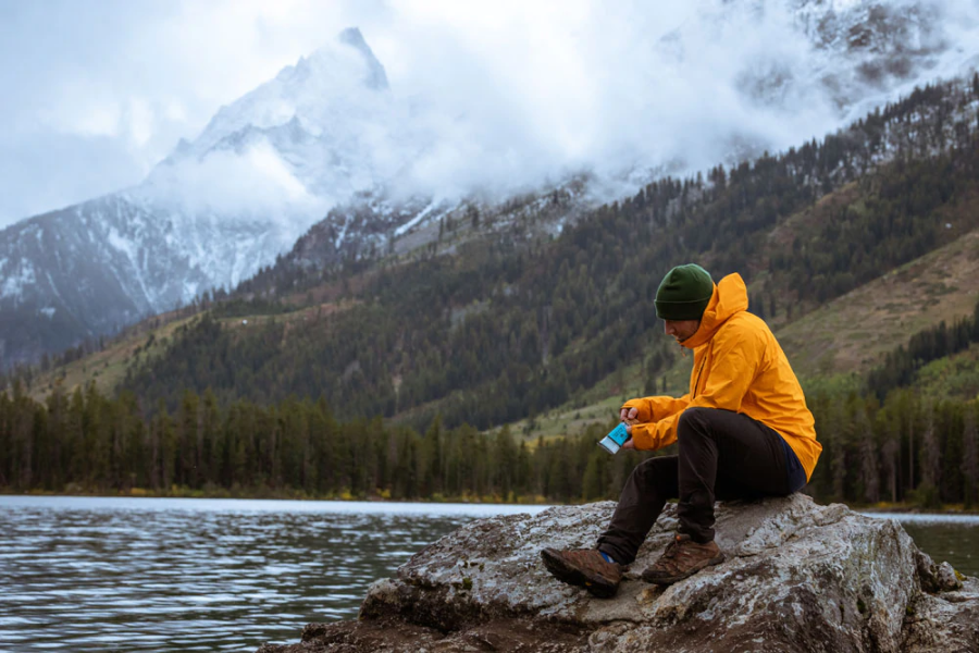 Man On Rock At Lake In Mountains Opening A Kate's PB Hemp & Flax Granola Bar Snack