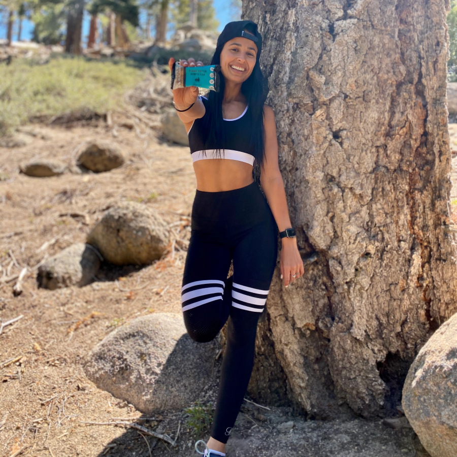 Woman Outdoors By Tree After Exercising Holding A Peanut Butter Hemp Flax Kate's Real Food Energy Bar